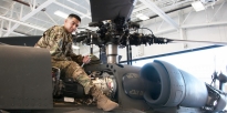 Soldier repairing a Apache helicopter inside a hangar during the daytime.